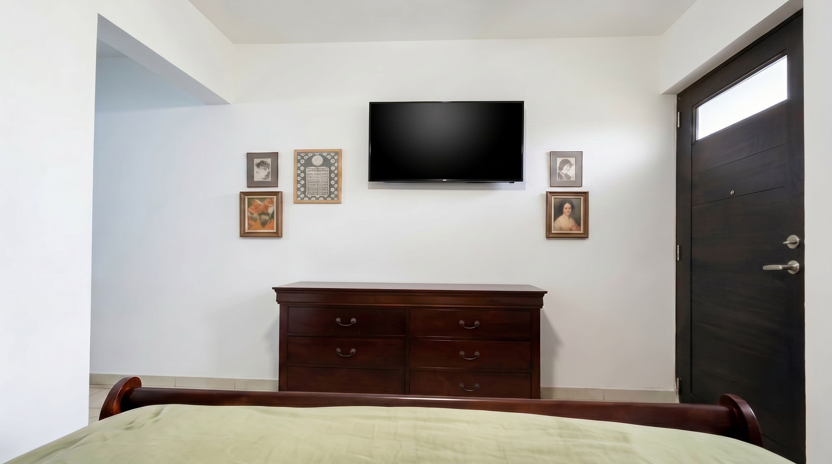 A bedroom with a bed, a dresser, a television, and a door.