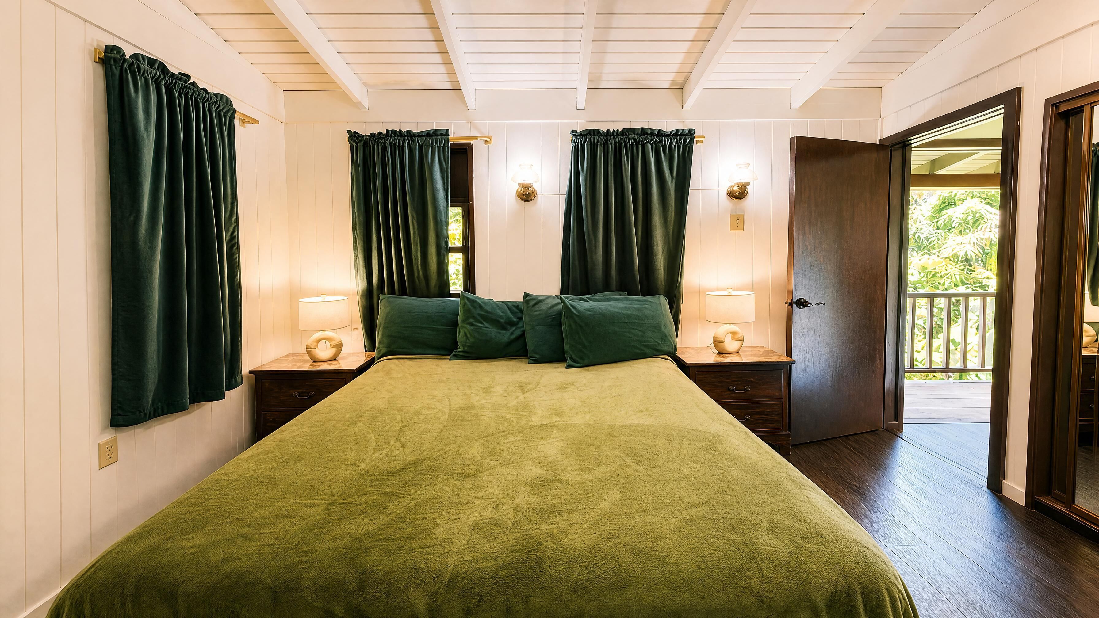 Un dormitorio con cubrecama verde, dos lámparas de noche y una puerta que da a un espacio exterior.