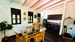 A dining area with a glass table and wooden chairs, a kitchen with dark cabinets, and a large mirror. - El Oasis Hotel (Aguada)