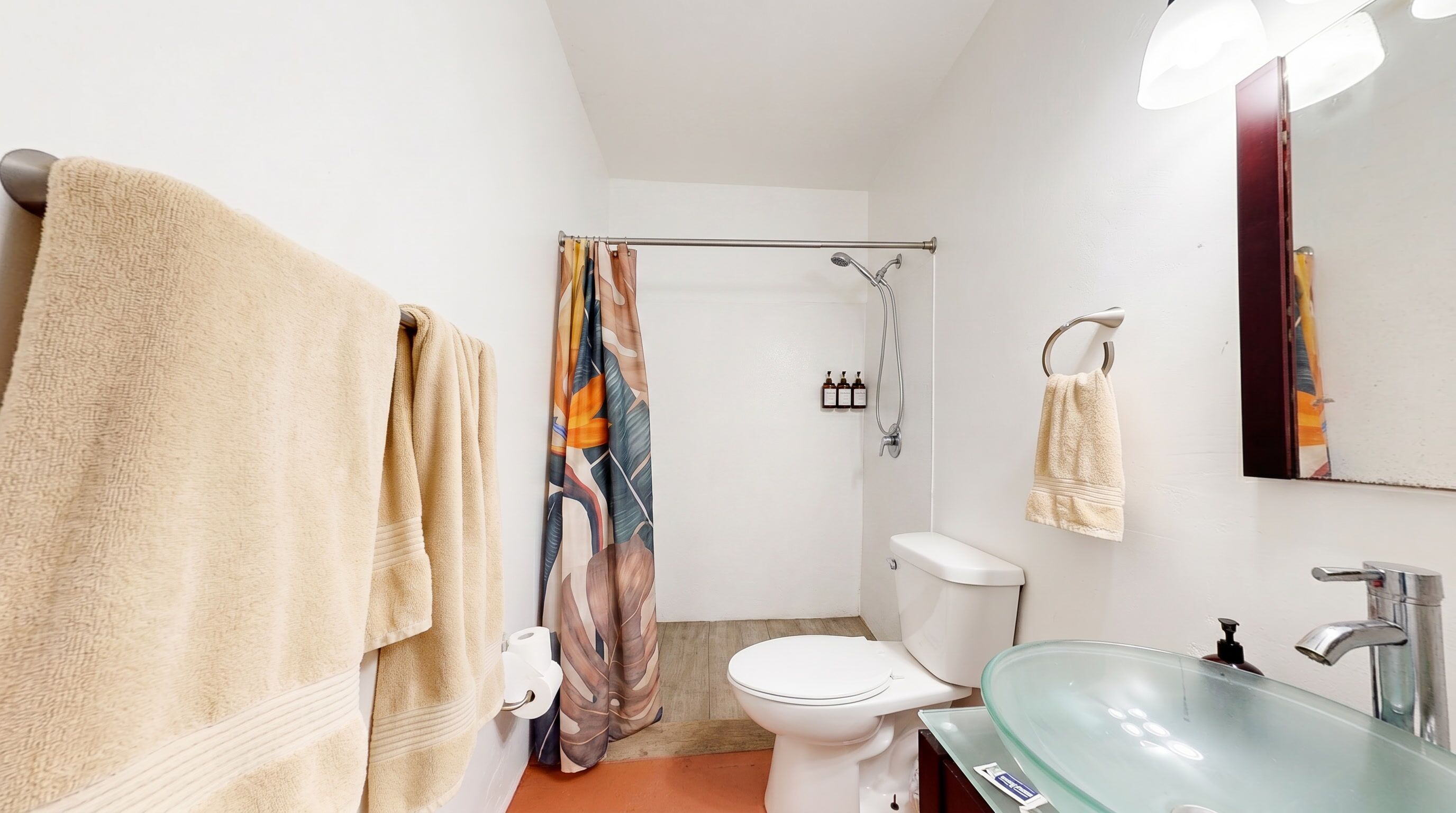 A bathroom with a toilet, a glass sink, a shower curtain, and towels.
