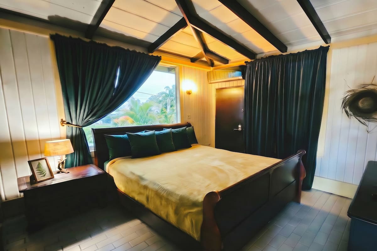 A bedroom with a bed, a nightstand, a lamp, a framed picture, a door, and a wall-mounted decoration.