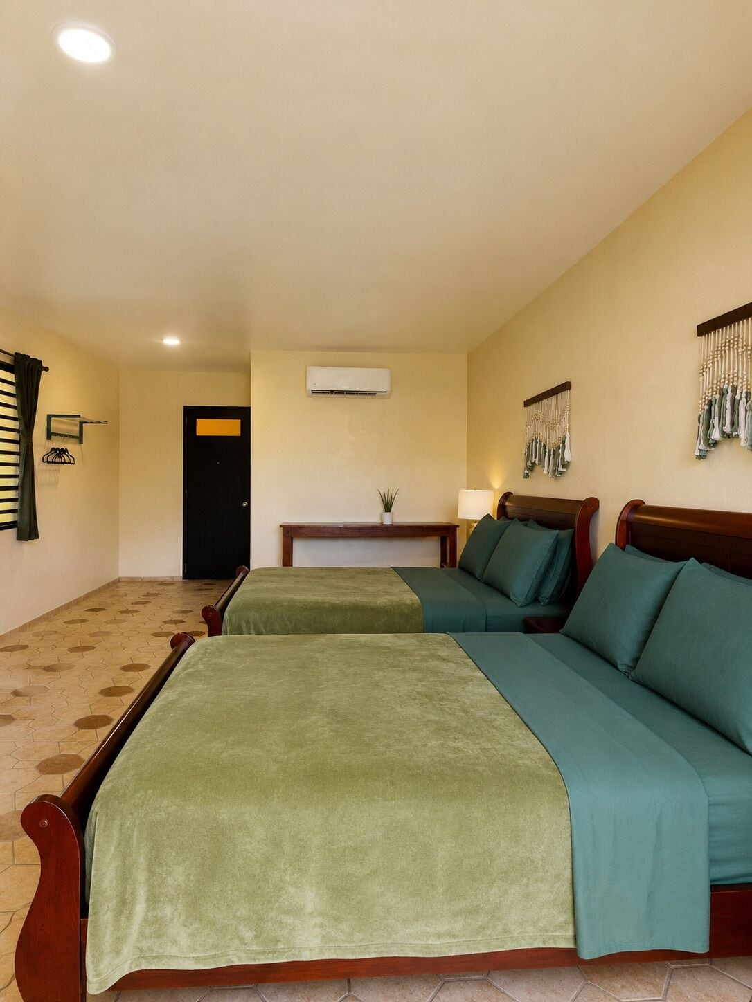 A hotel room with two beds, a small table, an air conditioning unit, a lamp, and a wall-mounted decorative item.