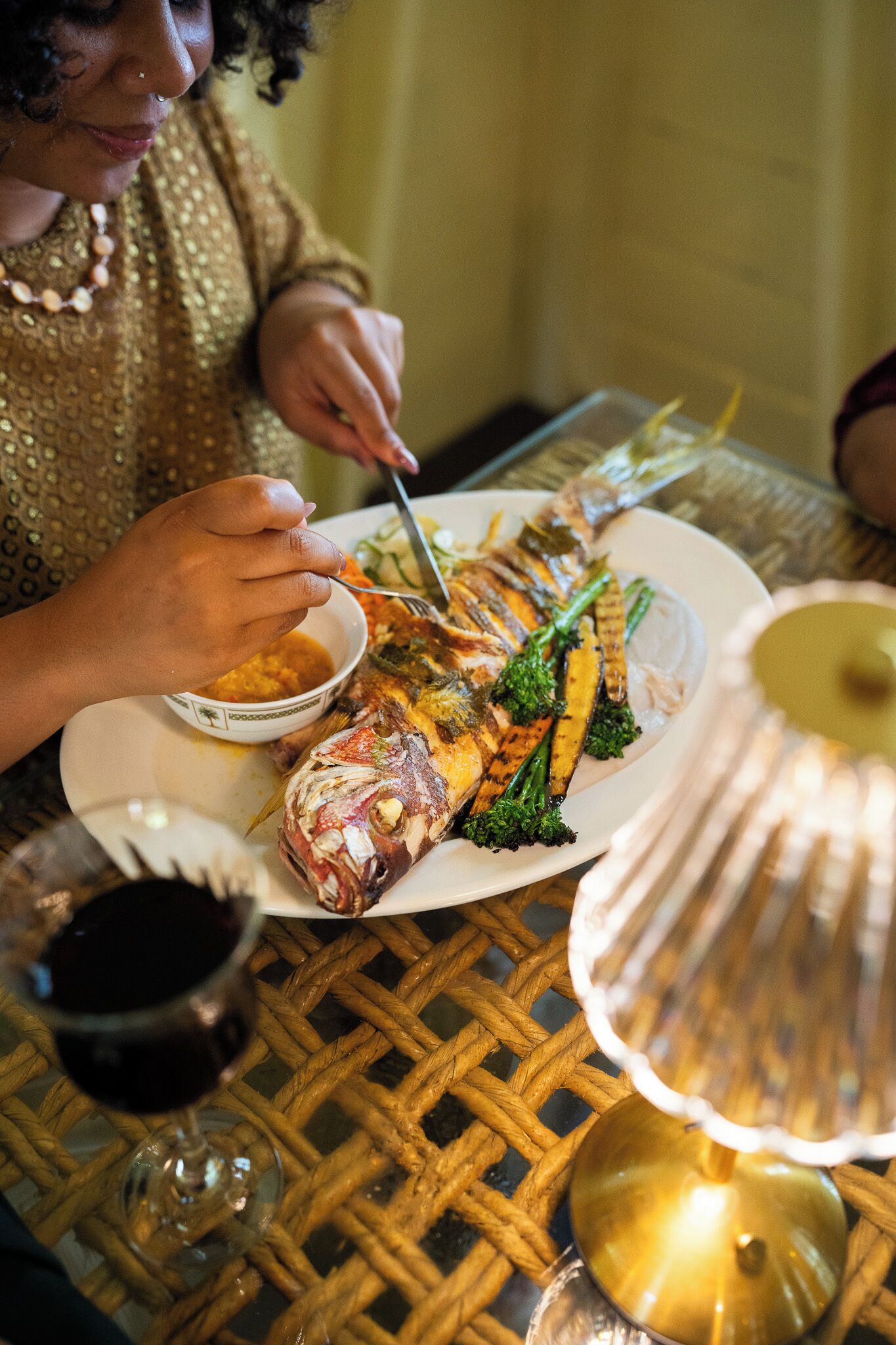Una mesa de comedor con un plato de pescado grande, un bol de salsa y una copa de vino.