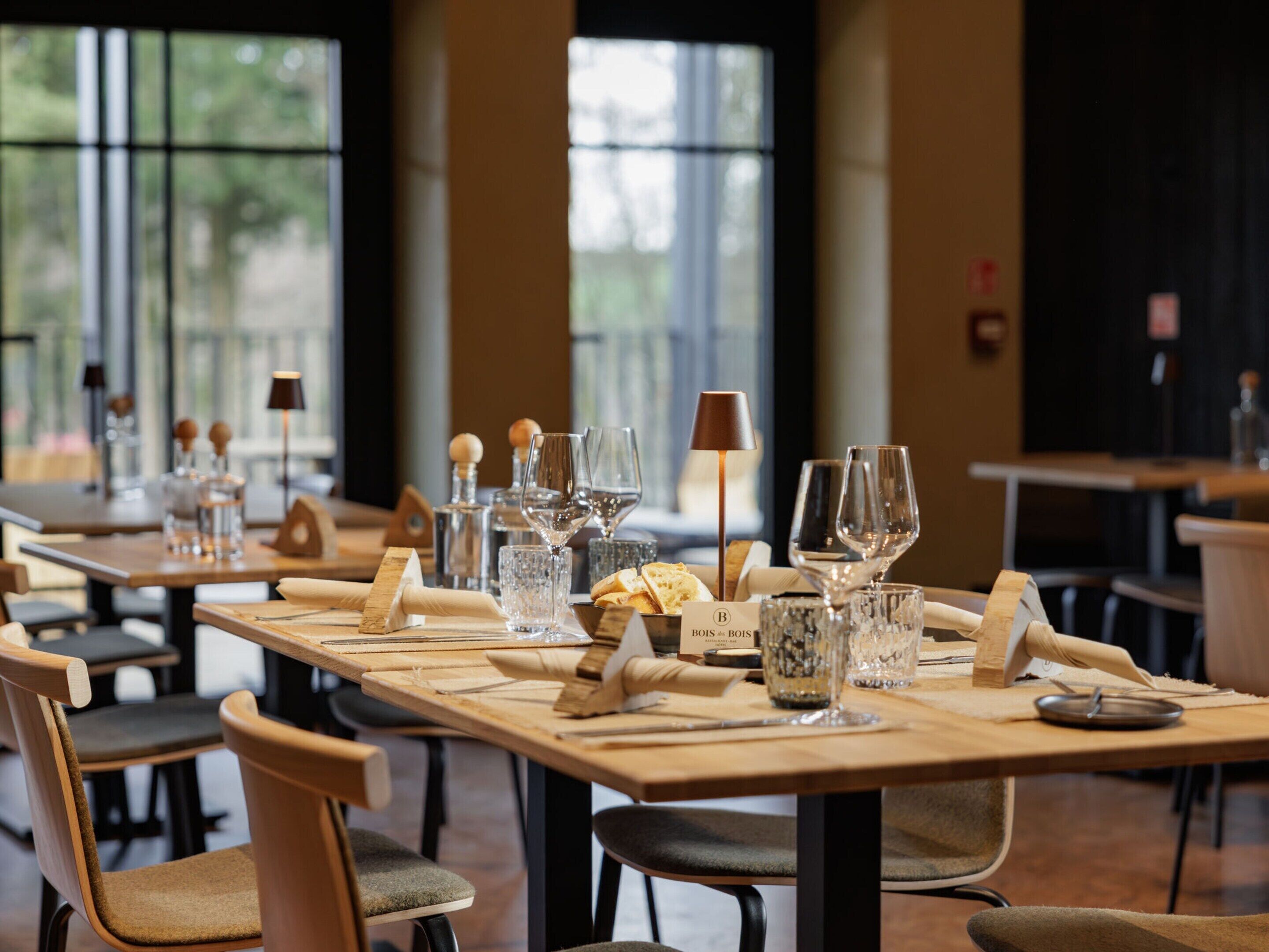 Un restaurante con mesas y sillas de madera, cristalería transparente y un cartel con el menú.