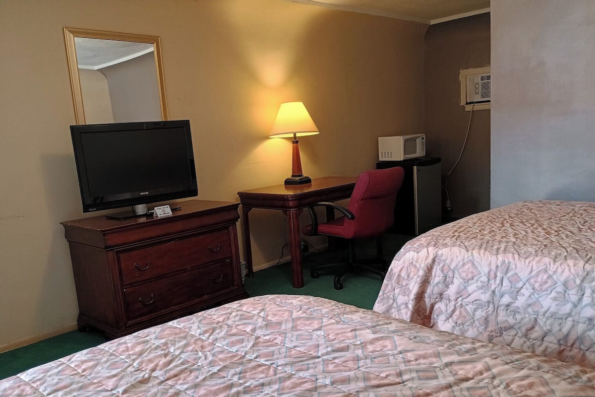 Une chambre d’hôtel avec deux lits, un bureau avec une chaise, une télévision, une lampe et un four à micro-ondes.
