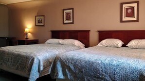 Una habitación de hotel con dos camas, una mesita de noche con lámpara y cuadros en la pared.