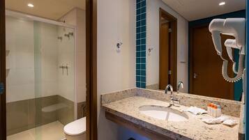 Un baño moderno con ducha de vidrio, lavamanos con encimera de mármol y secador de pelo montado en la pared.