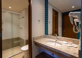 Un baño moderno con ducha de vidrio, lavamanos con encimera de mármol y secador de pelo montado en la pared.