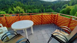 A terrace with a round table and chairs, surrounded by a wooden railing, overlooking a forested valley. - Schöne, große, barrierefreie Ferienwohnung, ruhig, idyllisch, familienfreundlich (Todtmoos)