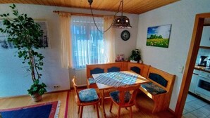 A cozy dining area with a wooden table and chairs, a hanging light fixture, and a view of the kitchen. - Schöne, große, barrierefreie Ferienwohnung, ruhig, idyllisch, familienfreundlich (Todtmoos)