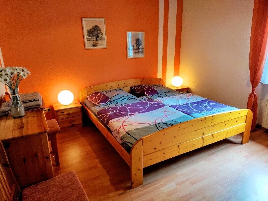 A bedroom with a wooden bed, two bedside tables, a nightstand, a vase with flowers, and two framed pictures on the wall.
