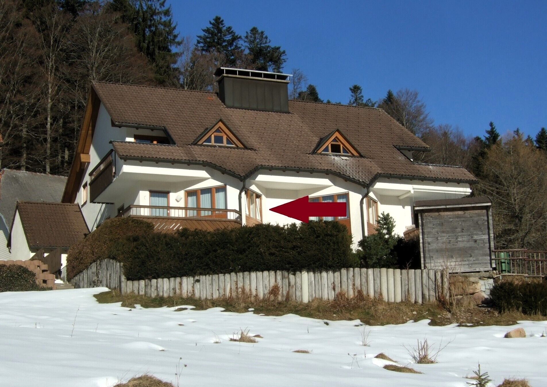 A two-story house with a sloped roof, a wooden fence, and a snow-covered ground.