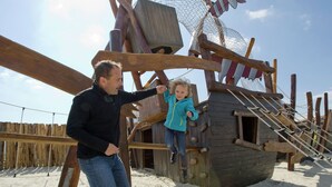 A wooden pirate ship structure with a ladder and a rope ladder on a sandy beach.