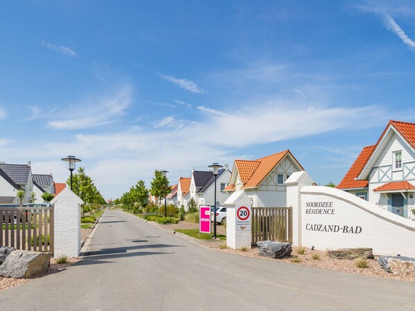 A residential area with white houses, a clear sky, and a road leading into the distance.
