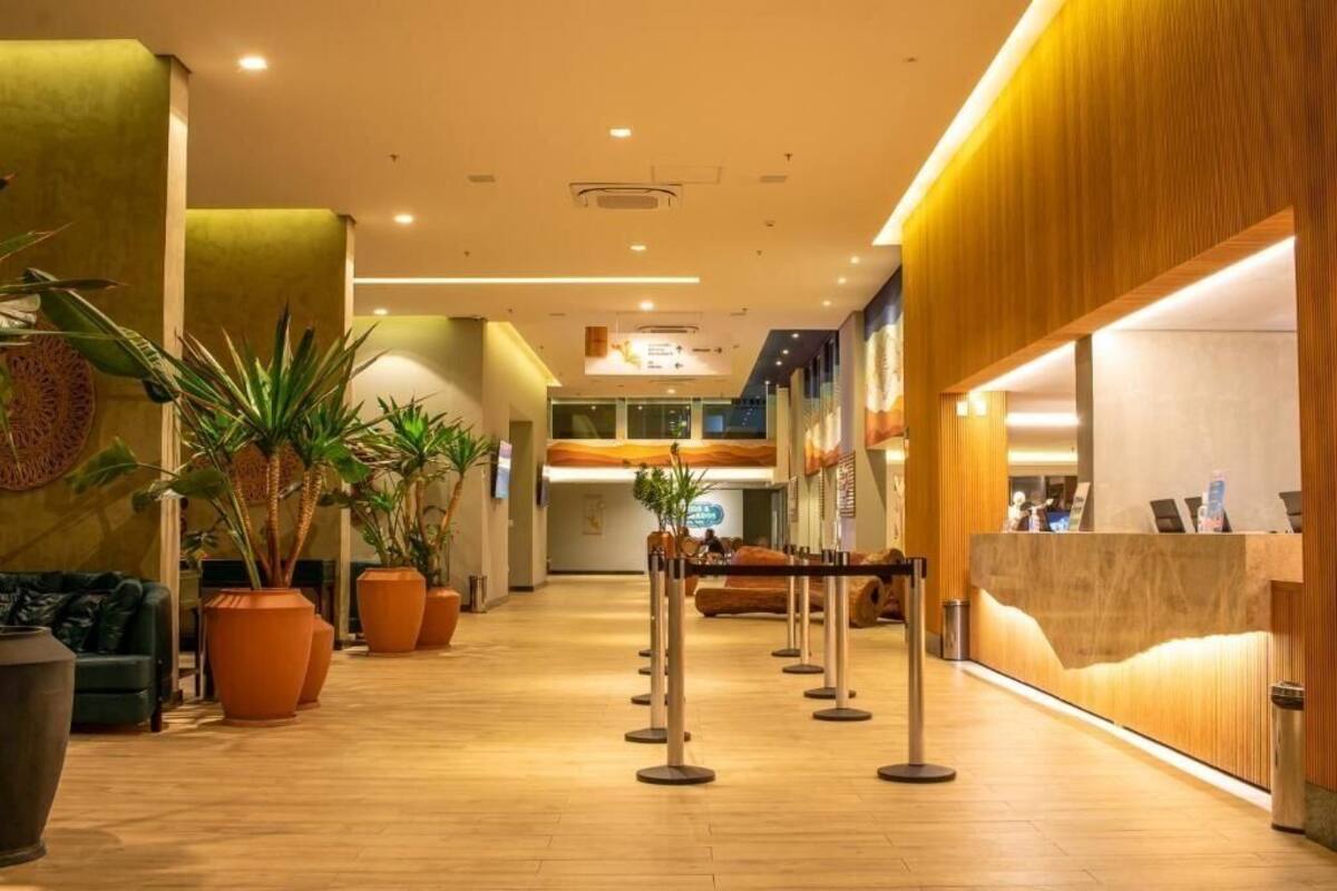 Een hotellobby met een houten receptiebalie, potplanten en een zithoek.