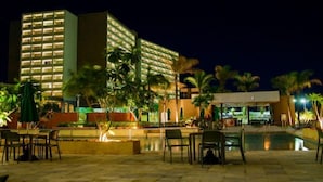 Ein Hotel mit mehreren Etagen, Außenbereich, Palmen und einem Pool.