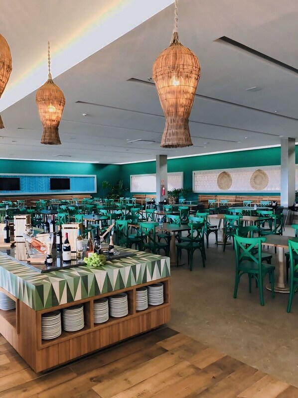 A spacious restaurant with green chairs and tables, a central bar area with a patterned tablecloth, and hanging wicker chandeliers. - Hot Beach Suítes Reserve Temporada (Olímpia)