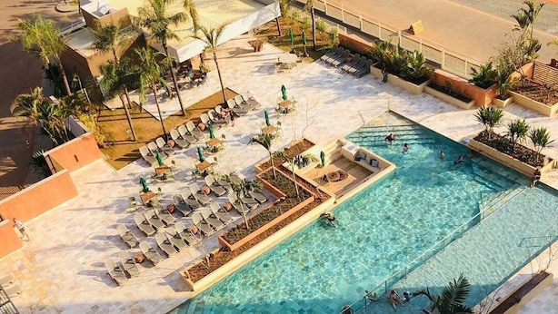 Ein Poolbereich auf dem Dach mit mehreren Liegestühlen, einem zentralen Schwimmbecken und umliegenden Palmen.