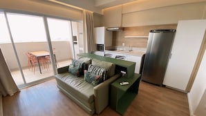Ein modernes Apartment mit einem grünen Sofa, einem Esstisch mit Stühlen, einer Küchenzeile und einer Glastür zum Balkon.