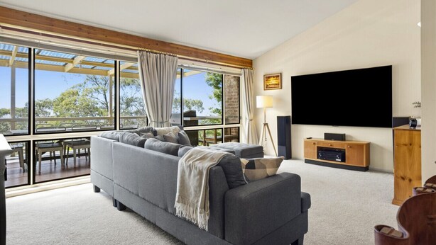 A modern living room with a grey sofa, a flat-screen TV, and a wooden TV stand. - Azimuth – Family Retreat with Sauna, Garden & Scenic Views (Wentworth Falls)
