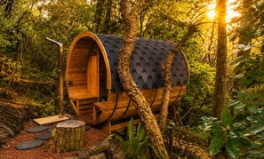 A wooden barrel-shaped structure with a staircase leading to a door, surrounded by trees and natural light. - Azimuth – Family Retreat with Sauna, Garden & Scenic Views (Wentworth Falls)