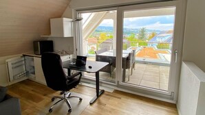 A small, open-plan room with a desk, chair, and a view through a sliding glass door.
