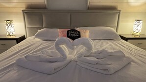 A neatly made bed with white linens and two towels arranged in a heart shape.