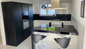 A modern kitchen with black cabinets, a stainless steel island, and two bar stools.