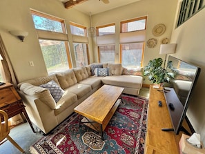 A living room with a sectional sofa, a wooden coffee table, a television, and a patterned rug.