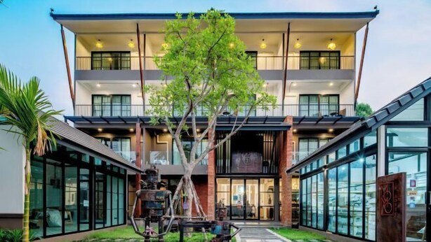 Um edifício moderno com um pátio central, grandes janelas de vidro e uma árvore no meio.