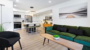 Een moderne leefruimte met een groene bank, een houten salontafel, en een keuken met witte kasten en roestvrijstalen apparatuur.