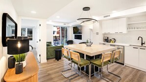 Een moderne keuken met een centraal eiland, witte kasten en een eethoek met groene bekleden stoelen.