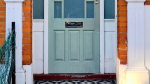 Un edificio tradicional de dos pisos con una puerta verde, columnas blancas y fachada de ladrillo.