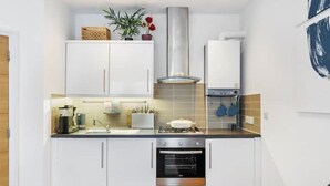 Una cocina compacta con armarios blancos, estufa, horno y un colgador para ollas.