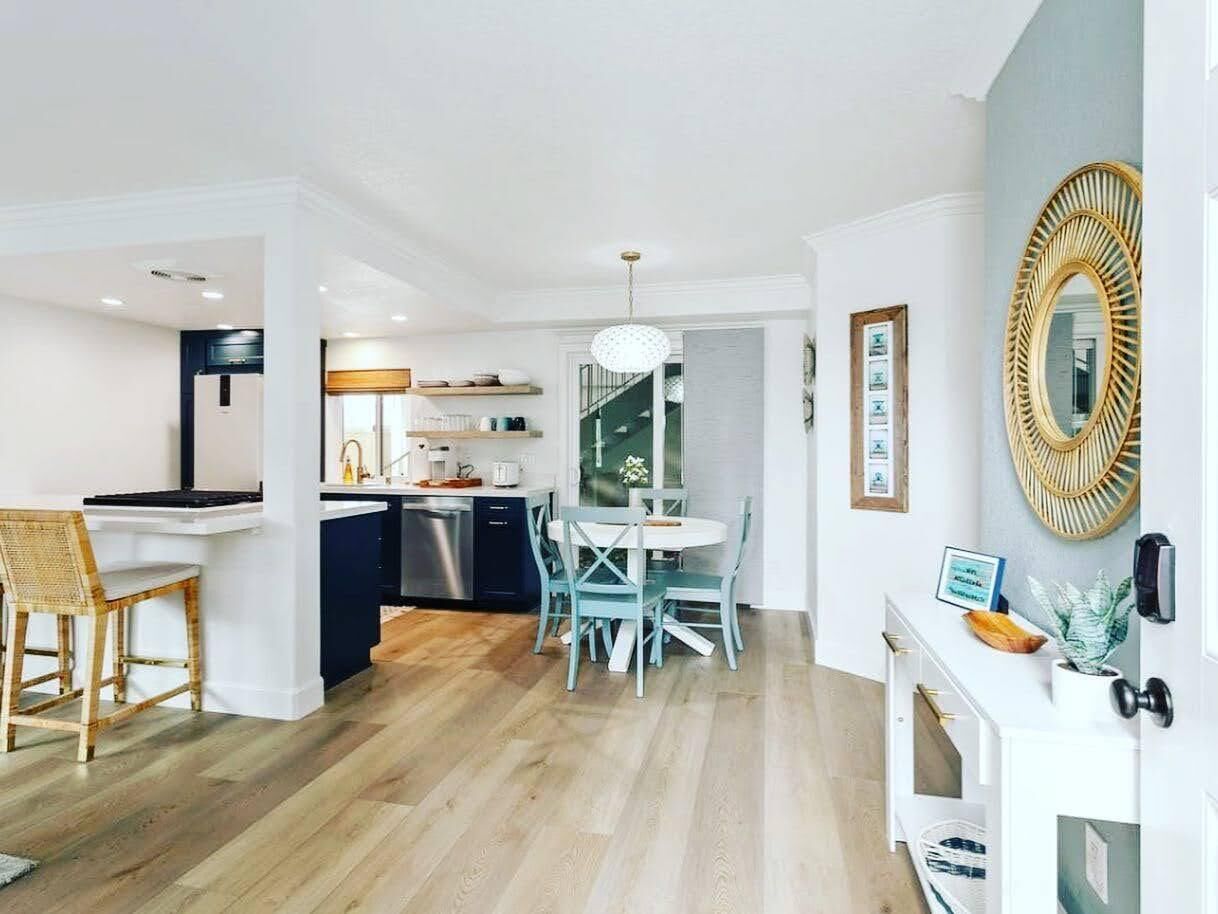 Une cuisine moderne avec un coin repas, un plancher en bois et un grand miroir au mur.