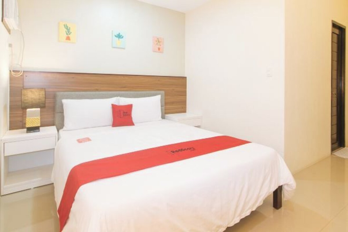 A hotel room with a bed, a nightstand, a lamp, and a red bedspread.