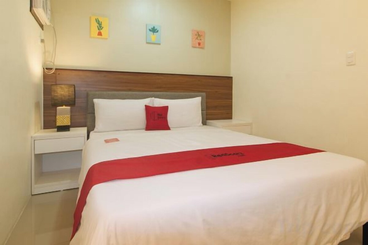 A hotel room with a bed, a nightstand, and a wall-mounted lamp.