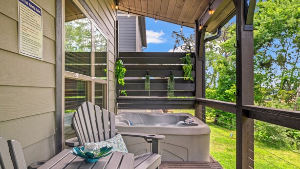 A hot tub on a wooden deck with a chair and table, surrounded by greenery. - Smoky Mountain Getaway • 2 King Suites • Hot Tub • Near Dollywood • Pets (Sevierville)