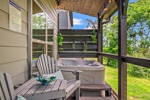 A hot tub on a wooden deck with a chair and table, surrounded by greenery.