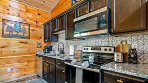 A modern kitchen with dark wooden cabinets, stainless steel appliances, and a patterned backsplash. - Smoky Mountain Getaway • 2 King Suites • Hot Tub • Near Dollywood • Pets (Sevierville)