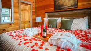 A wooden cabin room with a bed, a bottle of champagne, and a tray with glasses. - Smoky Mountain Getaway • 2 King Suites • Hot Tub • Near Dollywood • Pets (Sevierville)