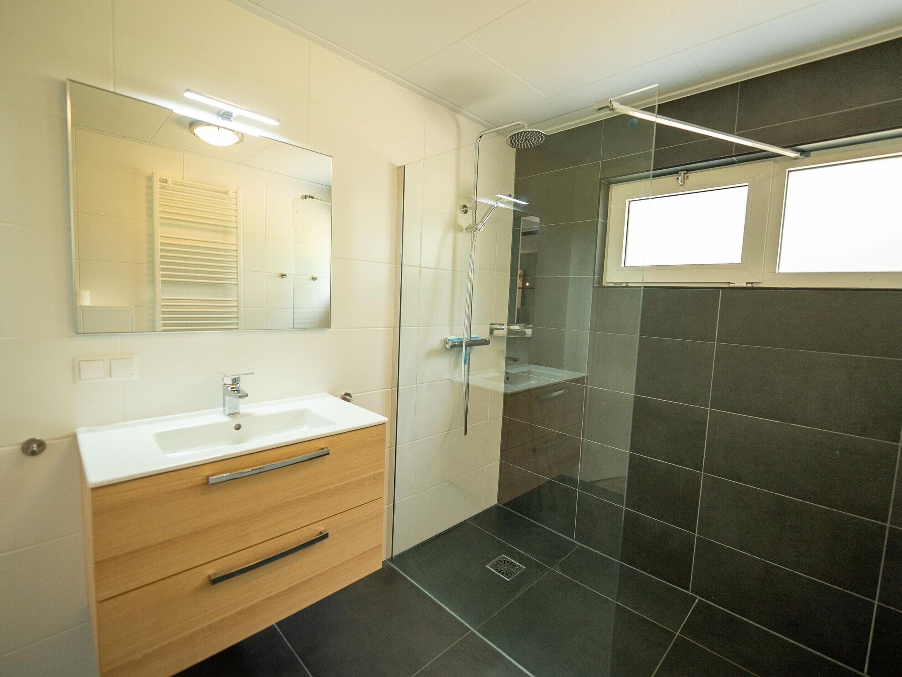 A modern bathroom with a white vanity, a glass shower enclosure, and a large mirror.