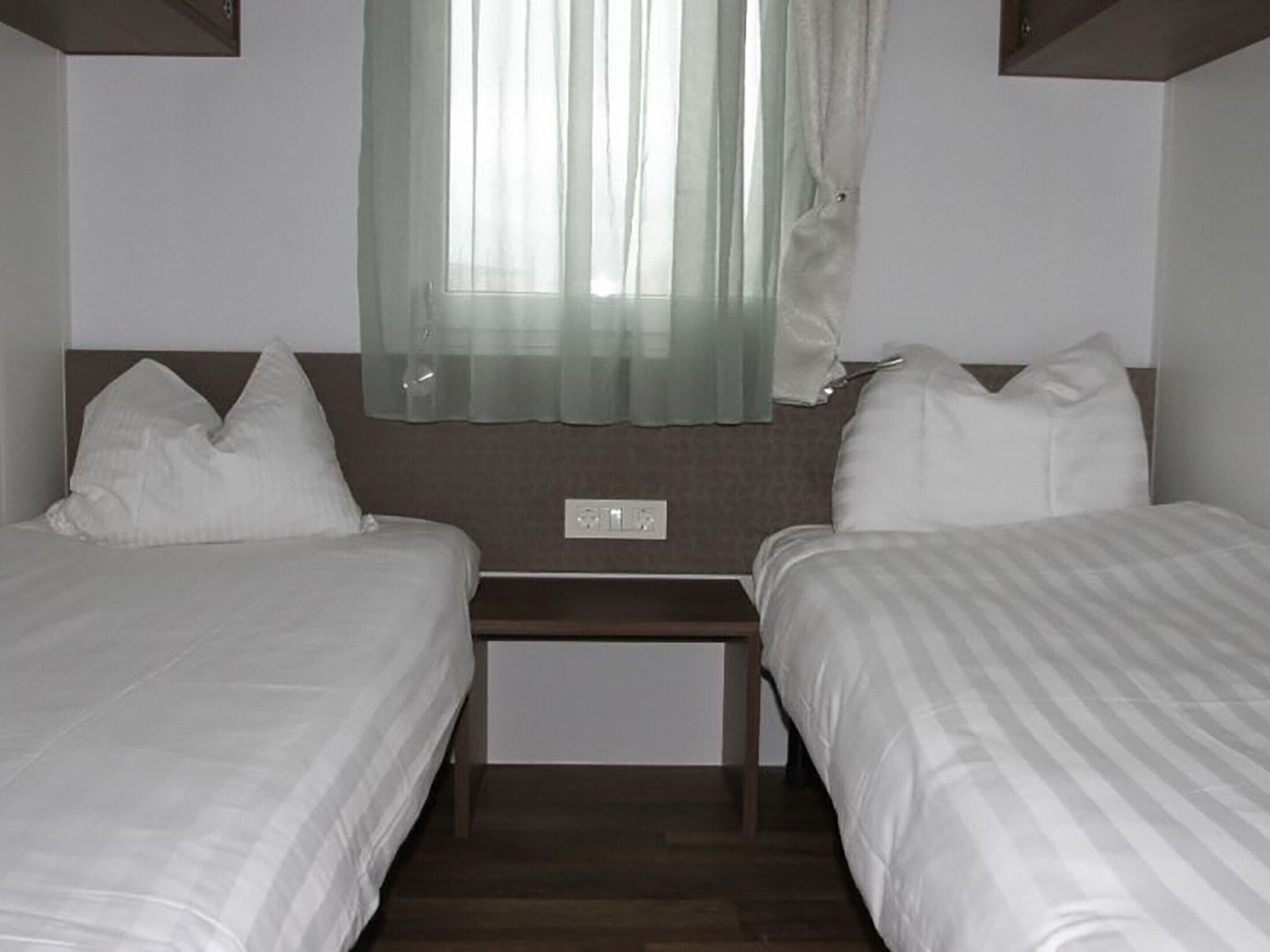 A twin room with two beds, a small table, and a window with sheer curtains.
