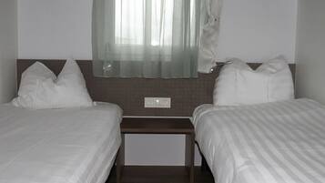 A twin room with two beds, a small table, and a window with sheer curtains.