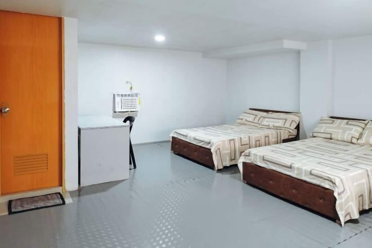 A room with two beds, a wooden door, a white radiator, and a wall-mounted heater.