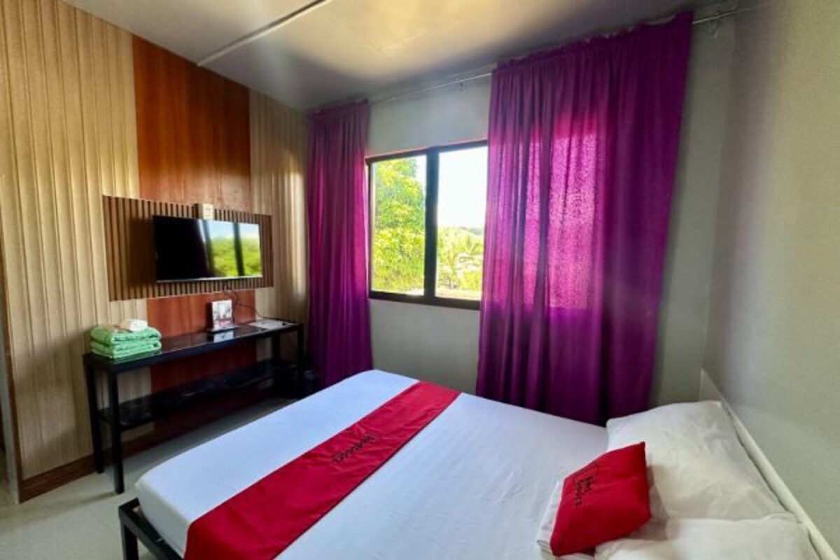 A hotel room with a bed, a desk with a television, and a window with curtains.