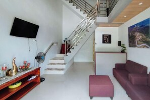 A modern living room with a staircase, a flat-screen TV, a sofa, and a coffee table. - RedDoorz @ FJ Hotel Tubungan Iloilo (Tubungan)