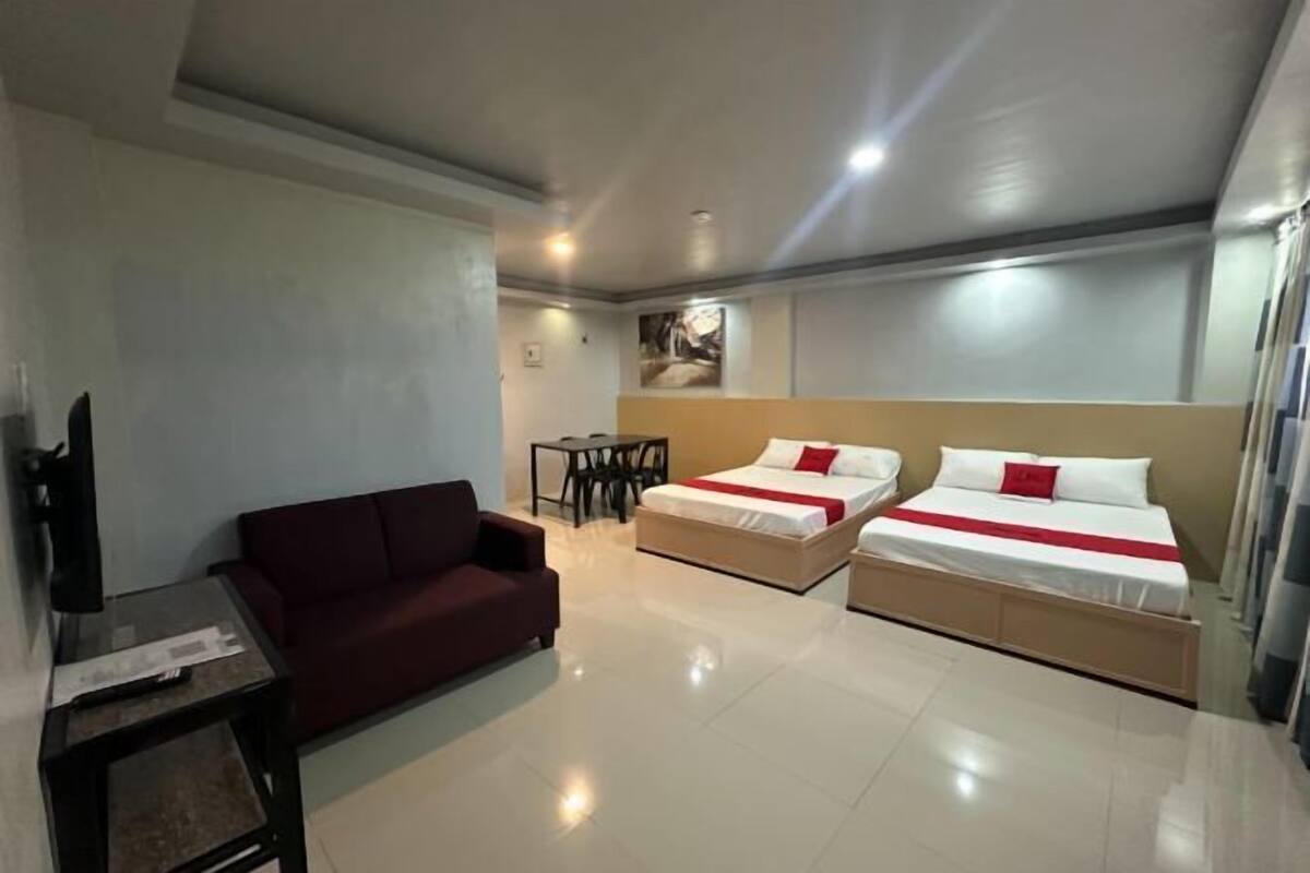 A hotel room with a sofa, two beds, a small table, and a TV.