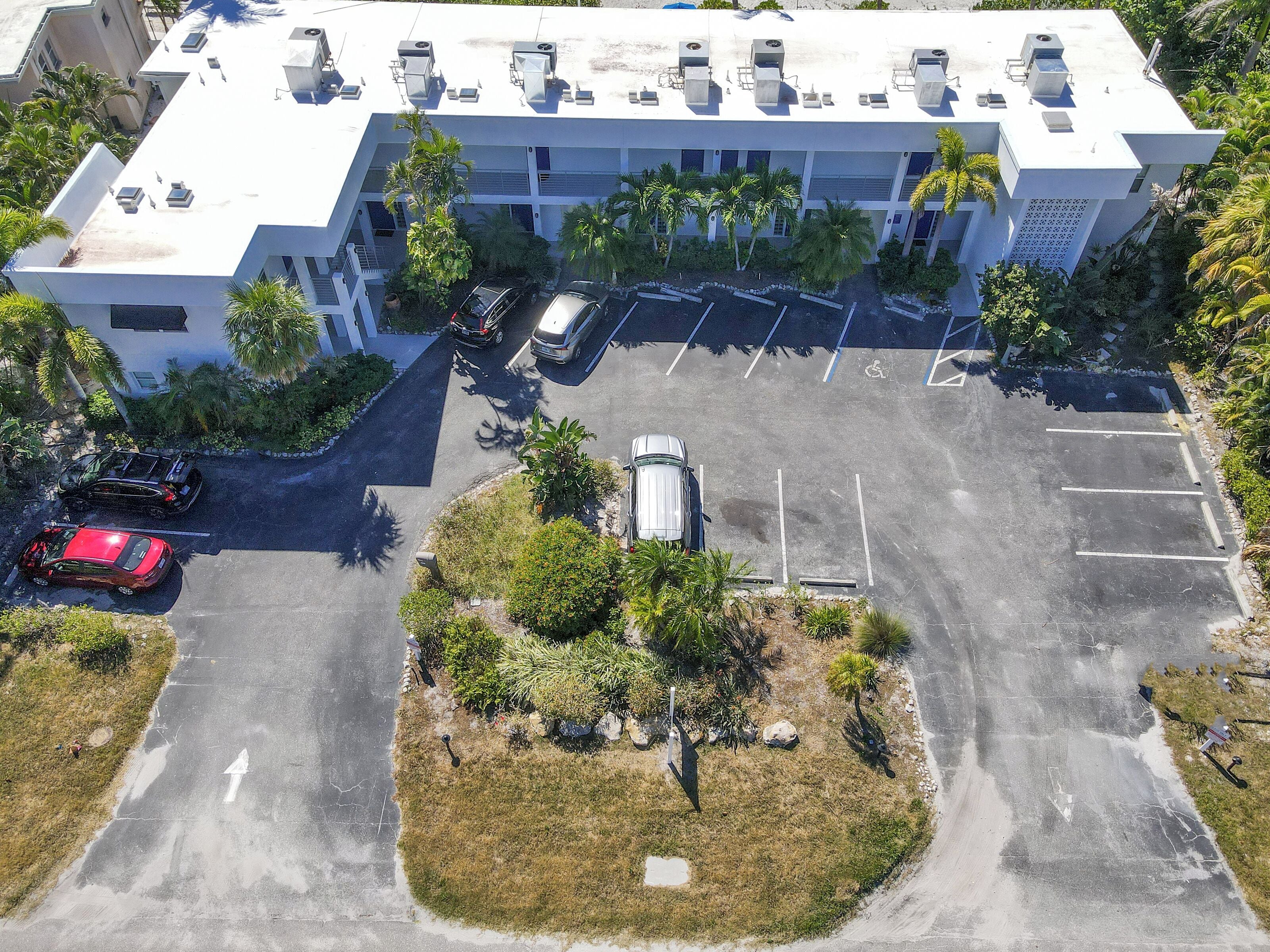 An aerial view of a modern building with a parking lot, surrounded by palm trees and greenery.
