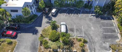 An aerial view of a modern building with a parking lot, surrounded by palm trees and greenery.